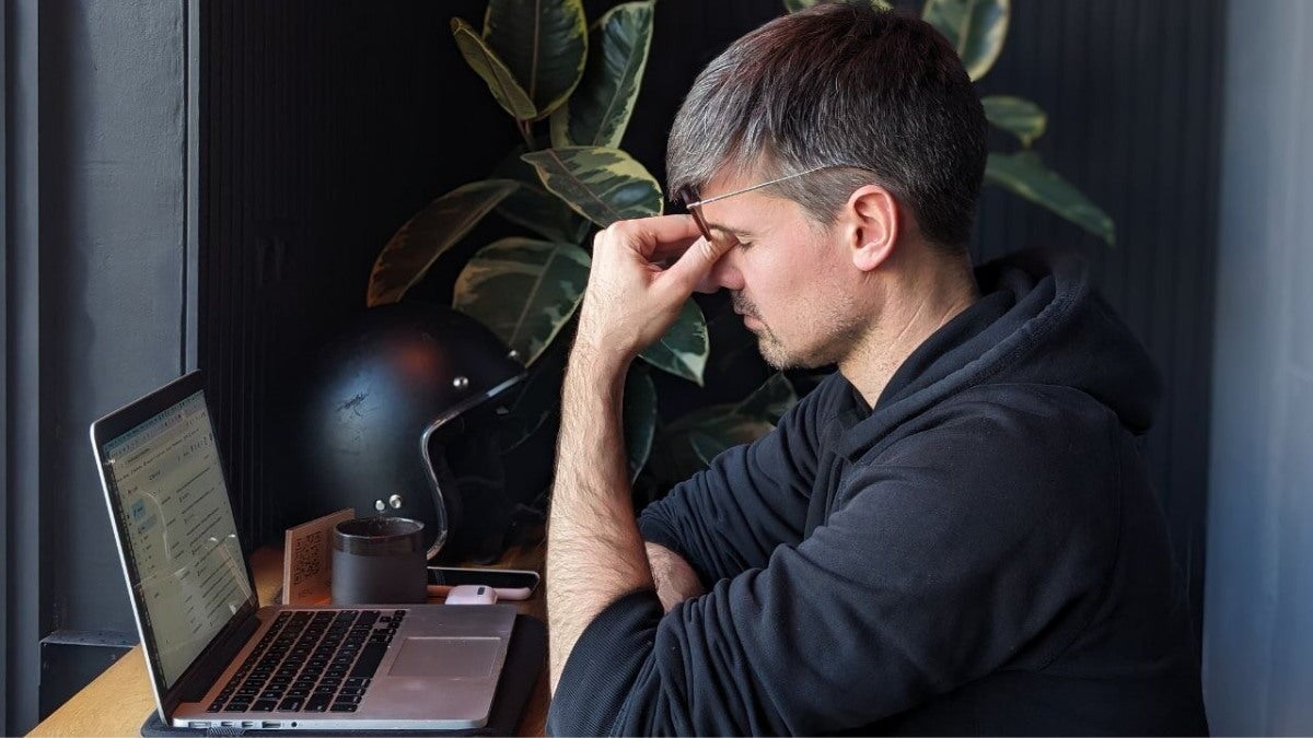 homme touchant ses yeux sous ses lunettes devant son ordinateur