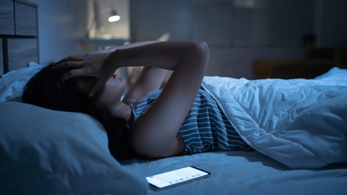 une femme au lit souffrant de manque de sommeil avec son téléphone à ses côtés